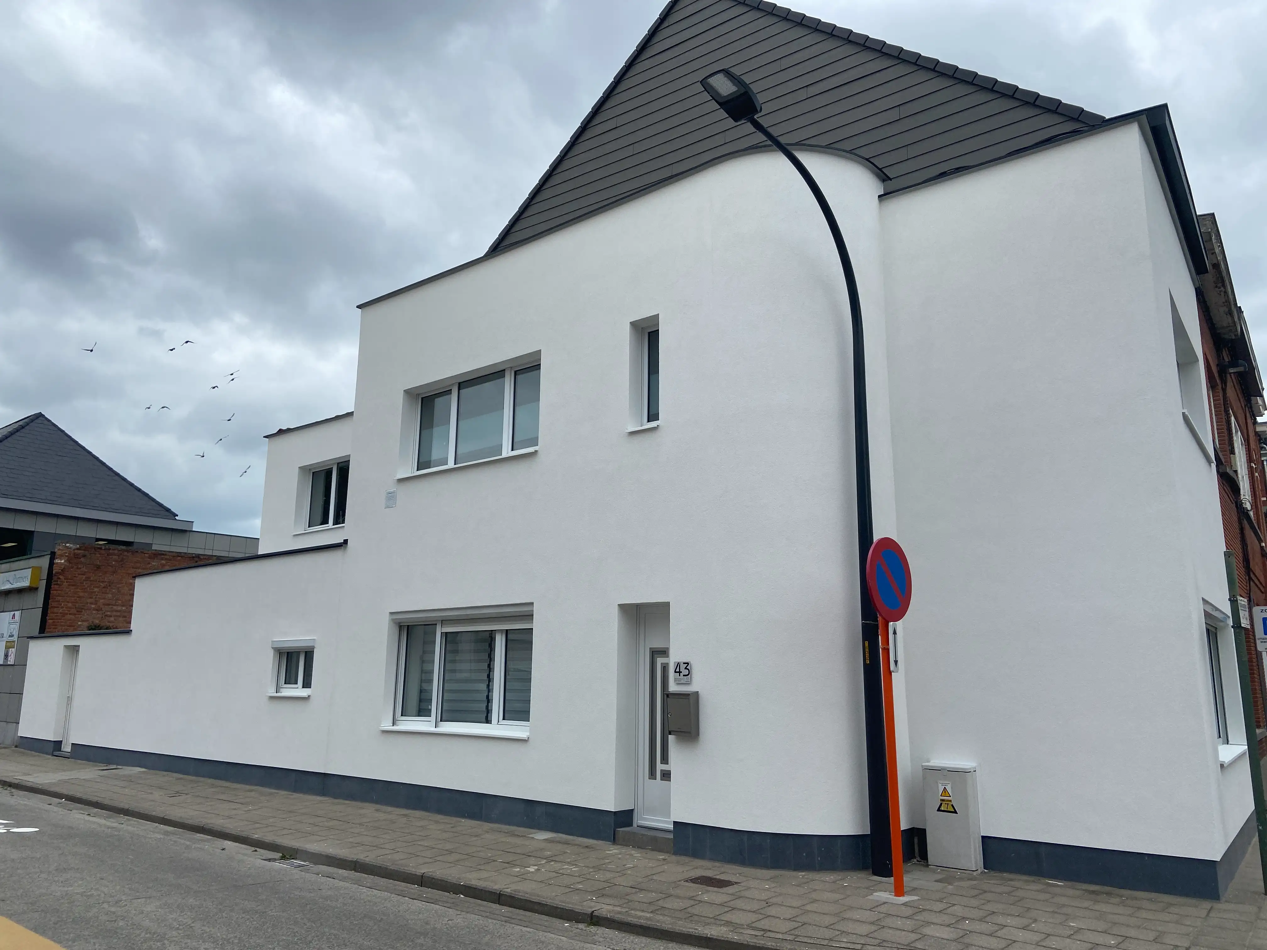 Moderne woning met witte crepi-gevel, meerdere ramen achter hoge gevels en een gebogen zijgevel onder een donker getiled zadeldak.