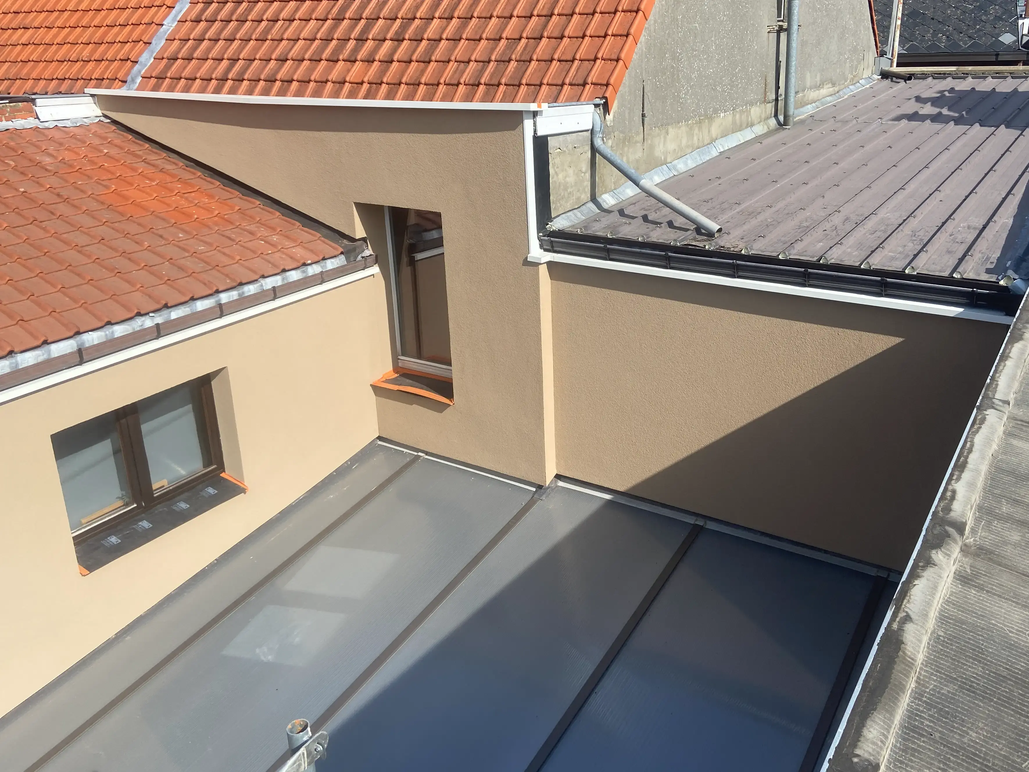 Hoek van een woning met nieuw aangebrachte beige crepi-gevel, omgeven door een rood pannendak en een grijs plat dak.