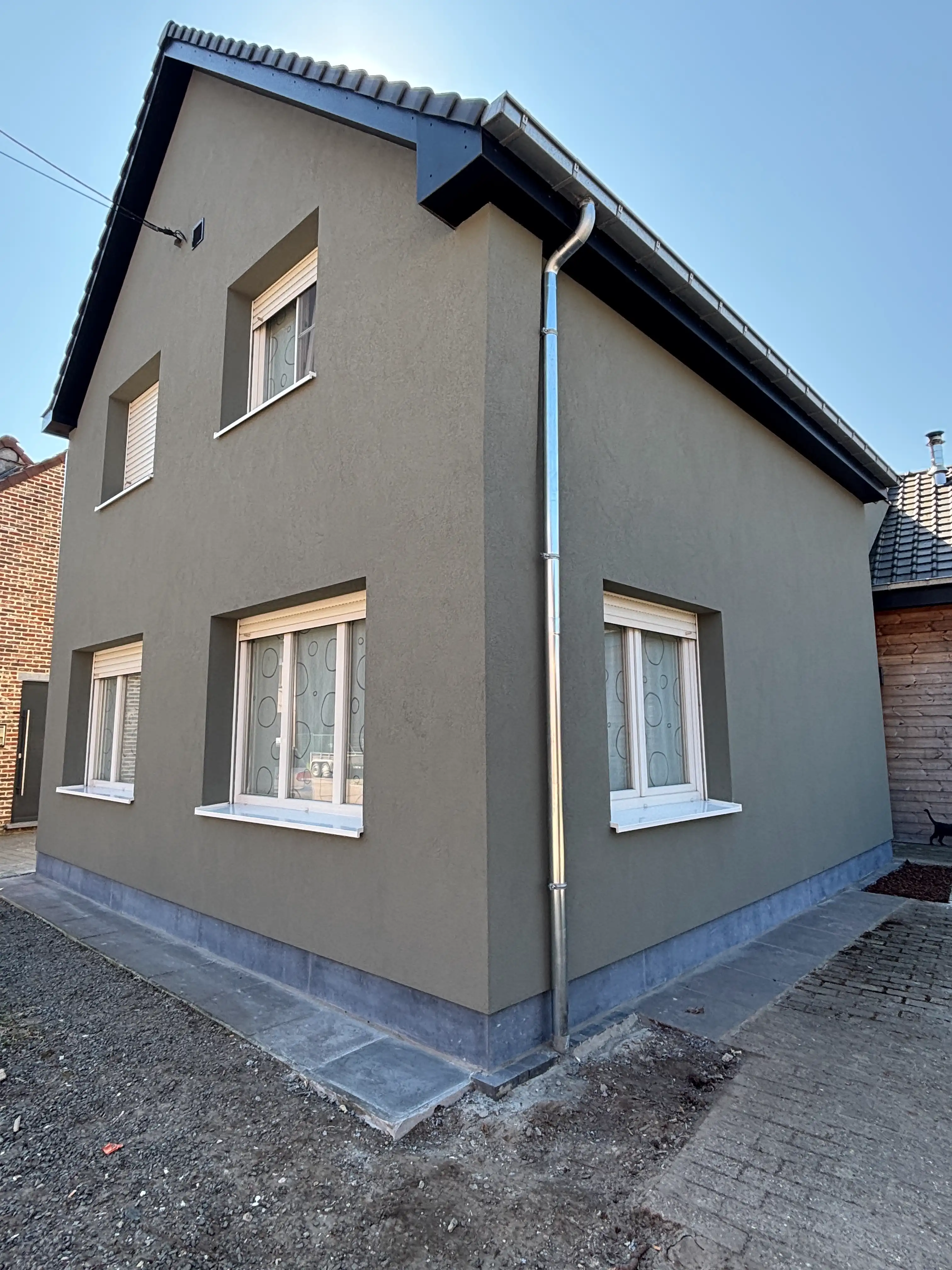 Hoekwoning met bruingrijze crepi-gevel, witte kozijnen, verzinkt regenpijp en donker getiled zadeldak.